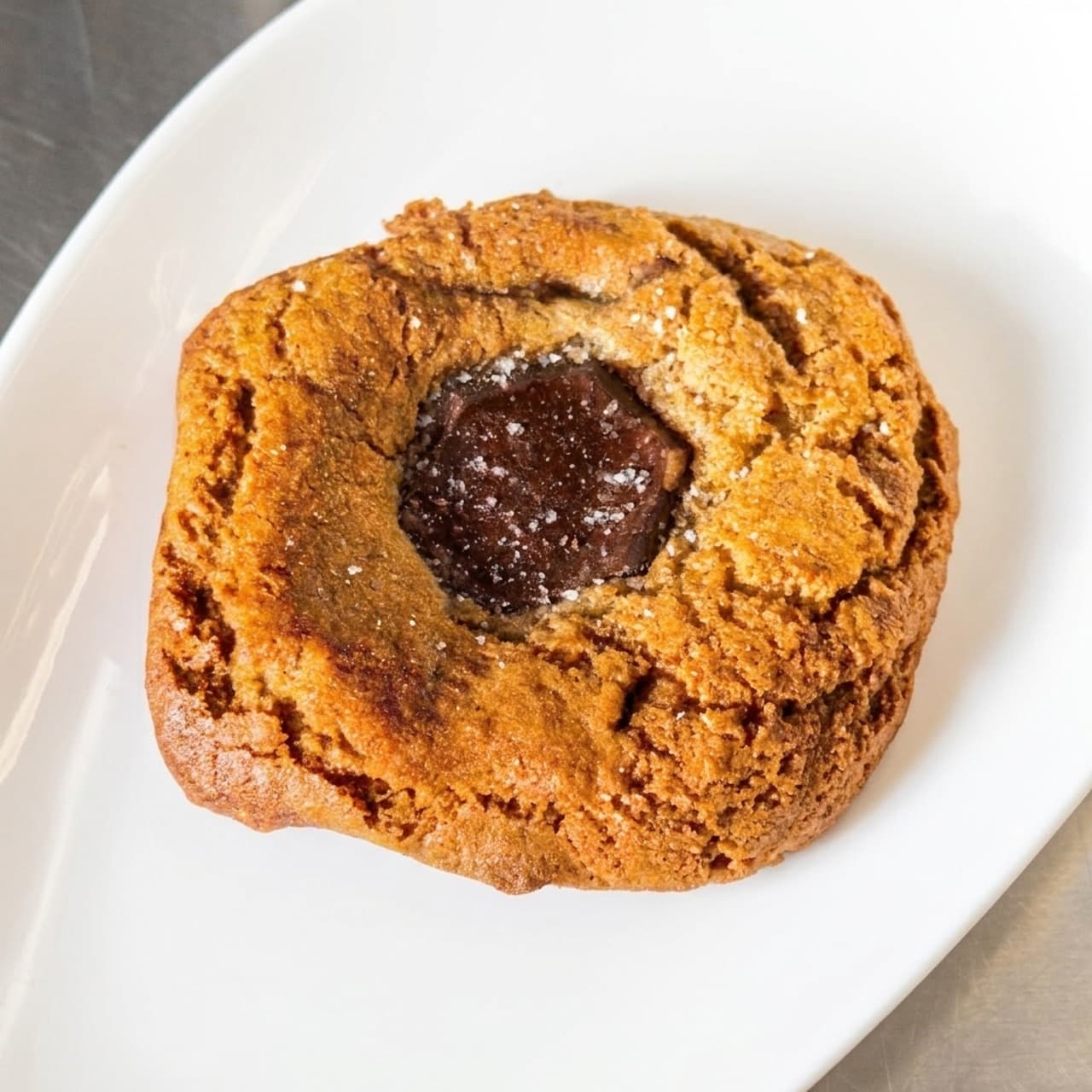 A thick Dark Chocolate Sea Salt Cookie on a white plate, with a hexagon of dark chocolate and flakes of salt on top